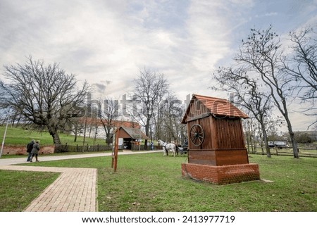 Traditional wooden wellhouse along the walkway at Szántódpuszta Majorság, Hungary - horse-drawn carriage in the background