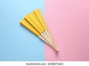 Traditional yellow Asian hand fan on pink blue background