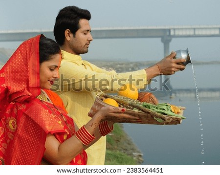 Traditionally dressed Indian couple worshiping God Sun - a celebration of Chhath Pooja festival, Bihari family, offering water. A man and a woman offering prasad to the Lord Sun on the occasion of ...
