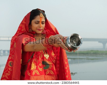 A traditionally dressed Indian woman in Chhath pooja attire is worshipping Lord Sun - Hindu festival, offering water. A woman standing in a river giving Argya to Lord Sun - praying to god, celebrat...