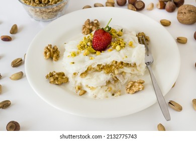 Traditionelles türkisches Ramadan Dessert Gullac, eine Portion auf weißem Teller mit Erdbeeren und Gabel und Walnüssen
