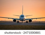 Traffic at airport at golden sunset. Front view of taxiing airplane while other taking off from the runway.
