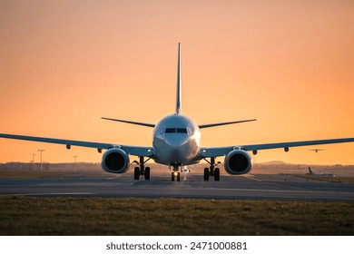 Traffic at airport at golden sunset. Front view of taxiing airplane while other taking off from the runway.
