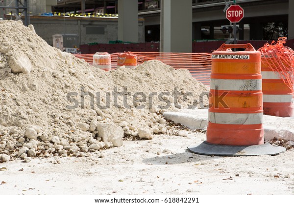 A\
traffic barricade of orange barrels indicates a site of road\
construction work with pile of sand and road\
sign