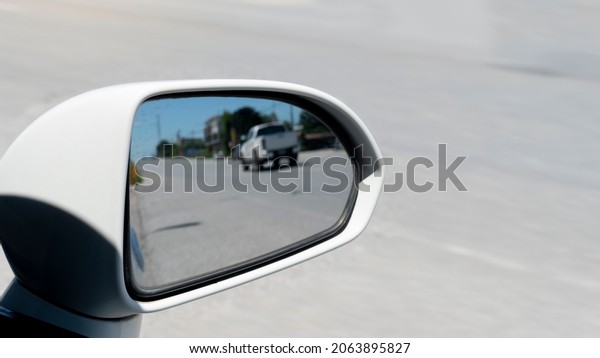 Traffic\
from behind through the mirrors wing of a white car. with blurred\
of other cars drving on the asphalt road at\
day.