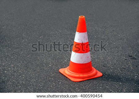 traffic cone, with white and orange stripes on gray asphalt, copy space