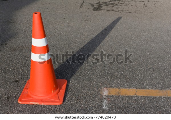 traffic cone, with white and orange stripes on\
gray asphalt.