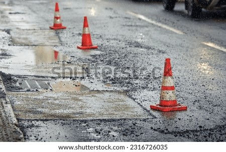 Traffic cones and asphalt pavement patching, removing pothole. Road repair work. Repair damaged road in the city. Pothole patching, laying new asphalt on damaged lane
