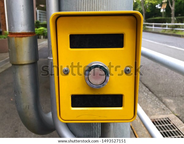 The traffic control button near a\
government primary school in Japan for helping students and\
pedestrians to stop the traffic sign when crossing the\
street.