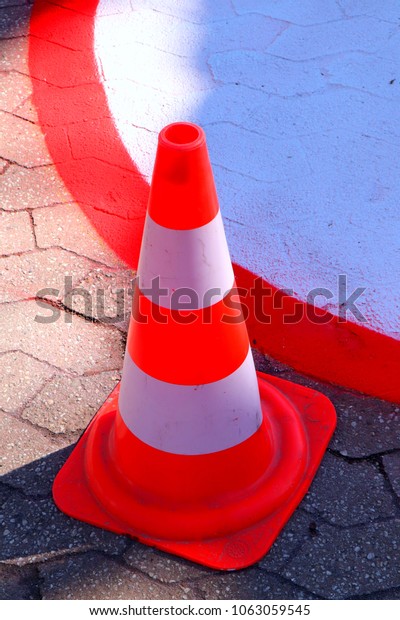 Traffic control neon red white striped plastic\
cone. Fragment of painted street sign in circle shape on the\
concrete tiled floor.