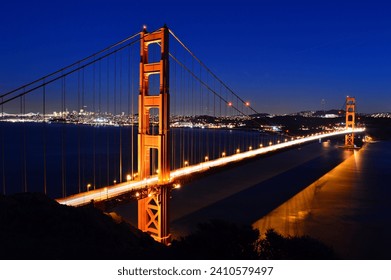 Traffic cruises across the Golden Gate Bridge in San Francisco as the bridge's lights are reflected in the water - Powered by Shutterstock