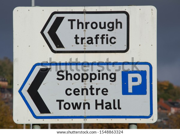 Traffic\
direction sign for through traffic, shopping centre parking and\
town hall, black text on white with black\
arrows