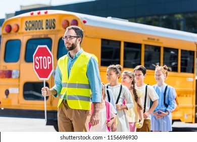 Traffic Guard Crossing Road With Schoolchildren In Front Of School Bus