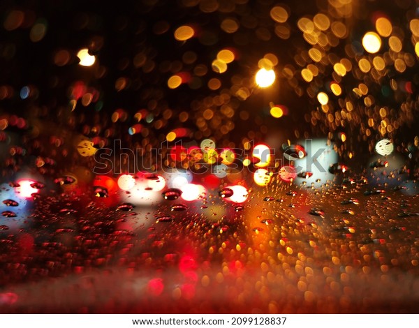 Traffic light\
bokeh with rain drops. Reflections of raindrops on glass on car\
window. Raindrops drizzle on glass window at night. Rain forecast\
for rain and weather. See\
Less