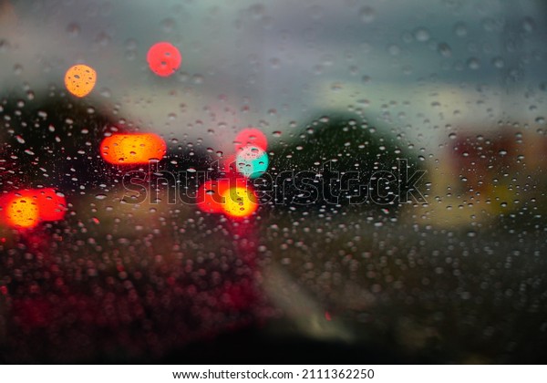 Traffic light bokeh with rain drops. Reflections of\
raindrops on glass on car window. Raindrops drizzle on glass window\
at night. 