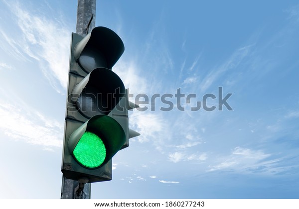 Traffic light in green color, with a blue sky\
and cloud in the\
background.
