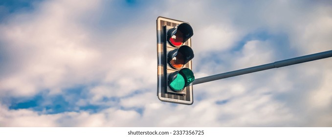A traffic light with a green light on a background of a blue sky with white clouds. Banner