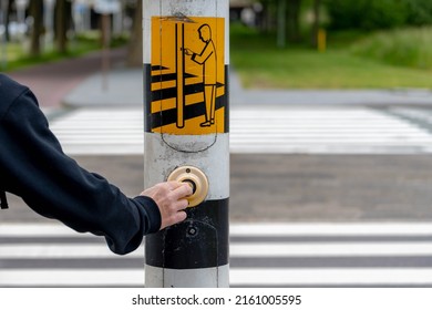 Traffic light, A man hand on the button of pedestrian on the pole while waiting for the red light, Press the button for green light before crossing on the road, Crosswalk in Amsterdam, Netherlands.