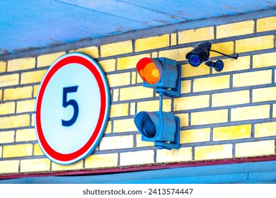 A traffic light with a monitoring camera on the garage wall above the garage door. Traffic signals regulate the entrance to a parking lot, underground parking lot or warehouse.