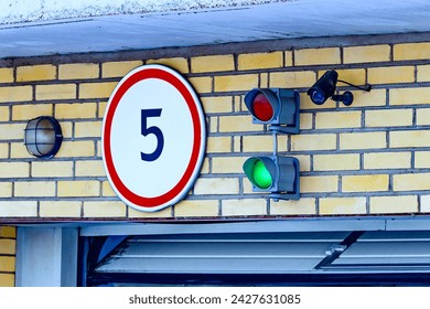 A traffic light with a monitoring camera on the garage wall above the garage door. Traffic signals regulate the entry and exit to a parking lot, underground parking lot or warehouse.green light.