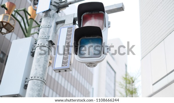 Traffic light pole with red and green sign\
near and blur building\
background