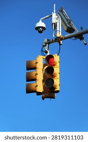 Traffic Light with Security CCTV Camera Against Clear Blue Sky. Traffic signal light showing red against a vivid clear blue sky, mounted on a metal pole alongside a dome security surveillance camera and wireless communication equipment. Modern intersection infrastructure combining traffic control and monitoring technology, shot from a low upward angle with copy space