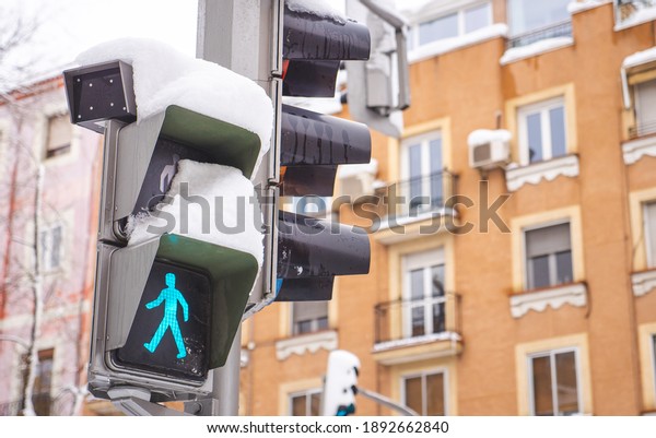 Traffic light\
with snow on a street in Madrid. The green crosswalk signal is on.\
Snowing during “Filomena” storm.\
