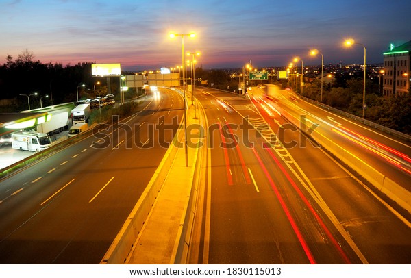 Traffic light trail a highway towards downtown of\
PRAGUE during night/twilight with reddish, purple and still blue\
sky. Signpost navigating to other cities and quarters,\
CZECHIA/Czech Republic,\
Europe