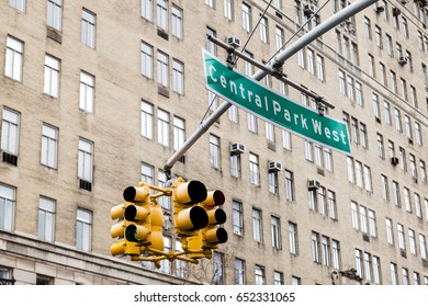 Traffic Lights And Green Overhead Street Sign Depicting It Is Central Park West In Manhattan, New-York, With A High Rise Residential Building In The Background.