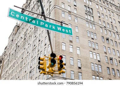 Traffic Lights And Green Overhead Street Sign Depicting It Is Central Park West In Manhattan, New-York, With A High Rise Residential Building In The Background.