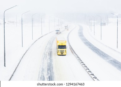 Traffic On The Highway In A Snow Blizzard. Cars On A Snowy Asphalt Road Ride In Dangerous Conditions With Poor Visibility And Strong Wind. Truck Transportation In A Winter Snow Storm And Cold Weather