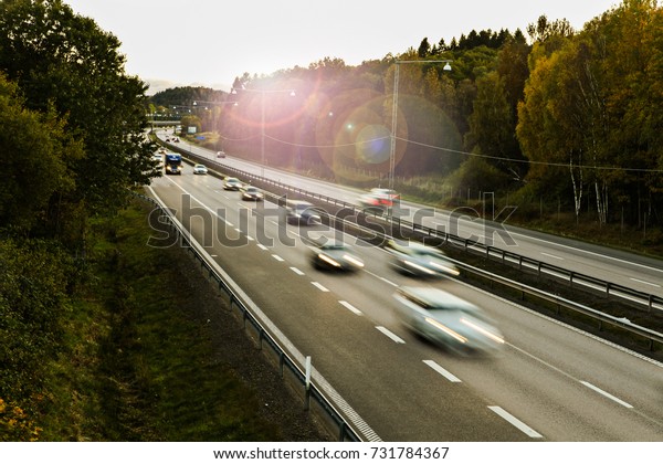 Traffic on a\
highway with two lanes in each direction in the evening. Cars going\
fast with motion blur. Lens\
flare