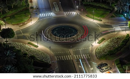 Traffic on a road intersection with roundabout in Greens district aerial night timelapse. Dubai skyline with many cars on a crossroad with fountain