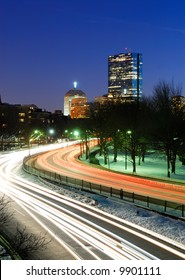 Traffic on Storrow Drive going in and out of downtown Boston at dusk. Car lights lead toward John Hancock Tower.