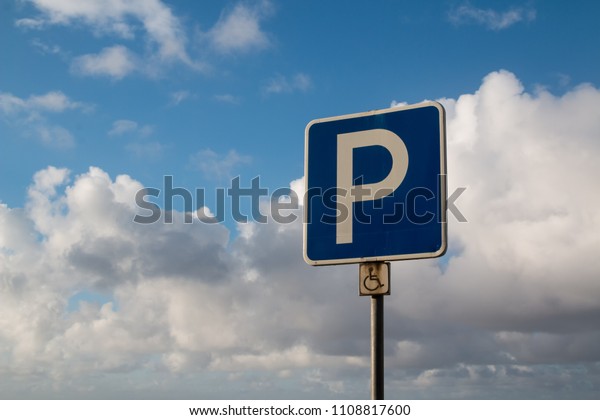 Traffic parking sign for disabled\
people. Intense white clouds on a blue sky after a night\
rain.
