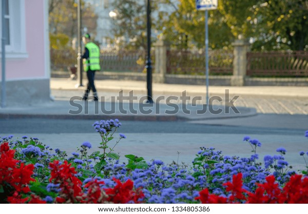 The traffic police inspector\
is doing his job. A man stands on a background of flower beds.\
Funny policeman loves flowers. Law enforcement on the\
streets.