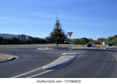 Traffic Roundabout In Australian City Of Coffs Harbour. In View Are Trees, Bitumen, Tar Road, Roundabout Sign Post, 'keep Left' Sign Post, Vehicles, Concrete Pavement Or Road Divider,  