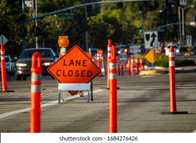 Traffic Sign In Diamond Shape Stating Lane Closed With Traffic Barrier Stantions In Foregound And Background 