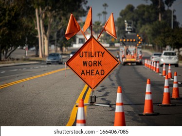 Traffic sign with flags reading Utilitary Work Ahead with traffic cones on road with electronic arrow pointing to the right to divert traffic