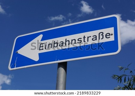 A traffic sign indicates a one-way street  Blue sign in front of blue summer sky with clouds  German traffic sign number 220-10 