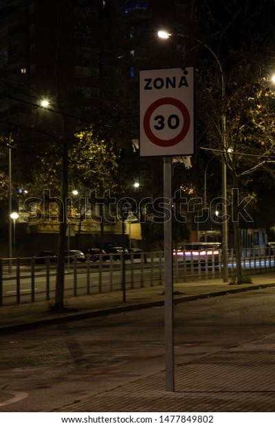 Traffic sign indicating low\
speed limit of 30 kph in urban area at night with copy space in\
Spain