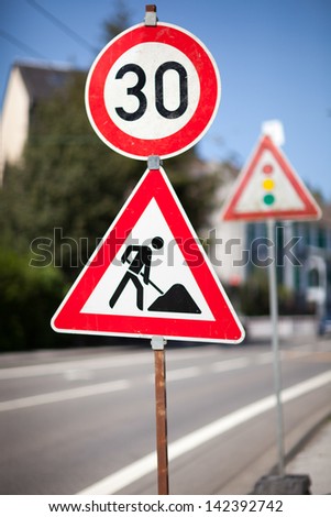 Traffic sign for roadworks ahead at the side of an urban road imposing a reduced speed limit