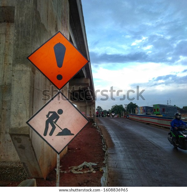 Traffic signs to be\
careful crossing because there are construction works on the\
background of buildings, roads, motorists and blue\
sky.Bekasi.Indonesia 8th Januari\
2020