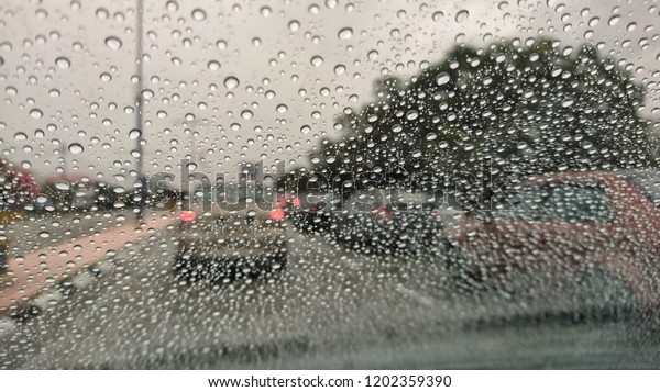 Traffic stands still, on a cold, wet day, shot through a\
windscreen, focusing on the rain droplets, tailights out of focus.\
