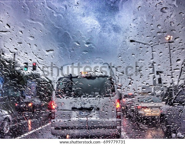Traffic stands still on a rainy day with road\
view through car window with rain\
drops