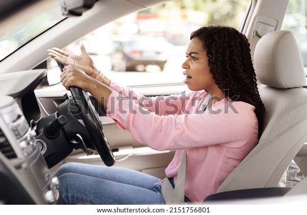 Traffic Stress. Angry female driving car shouting at\
somebody, emotionally reacting to accident or road jam holding\
steering wheel with displeased face expression, waving hand,\
profile side view