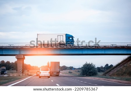 Traffic from trucks and cars on the road. A truck drives over a bridge against the backdrop of an evening sunset and blue sky. The concept of import and export, cargo turnover, sanctions for the trans