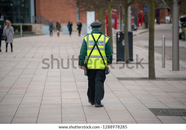 traffic warden civil enforcement officer wearing\
reflective yellow vest walks down the middle of the street\
completely alone