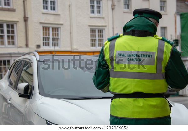 traffic warden civil enforcement officer wearing\
reflective yellow vest issuing fixed penalty parking ticket fine in\
typical UK high street