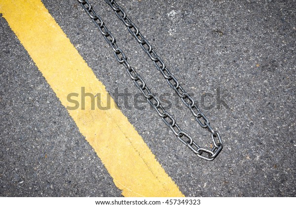 Traffic yellow line with metal chain on the\
asphalt floor - Conceptual\
background